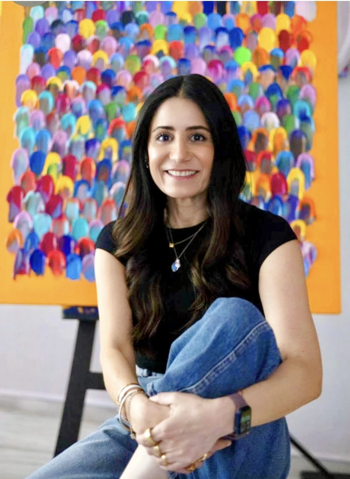Olinka Domínguez sentada en su estudio frente a una de sus pinturas